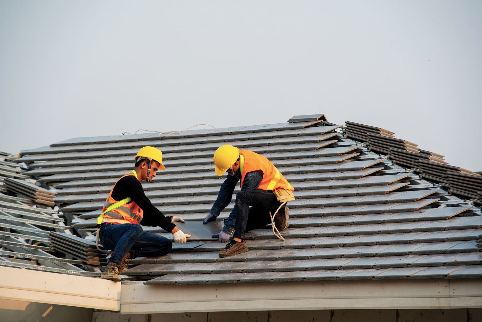 Two roofers in safety vests kneel on a shingle roof during an inspection
